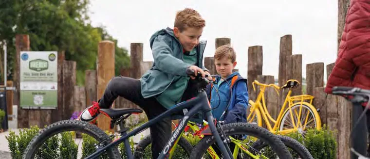 Children preparing hired bikes at a bike hire station beside a wooden fence