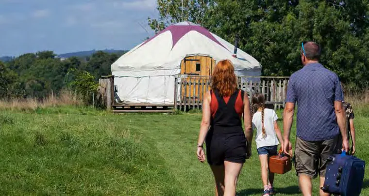 Family walking across a grassy field toward a white yurt at a Boyne Valley glamping site