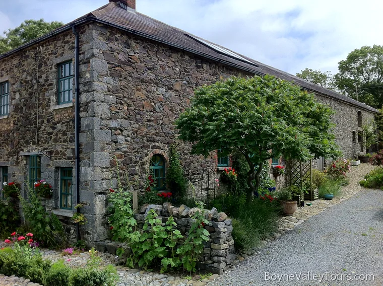 Stone coach house on the Ashbourne to Drogheda road at Duleek with green window frames, gravel drive and garden planting