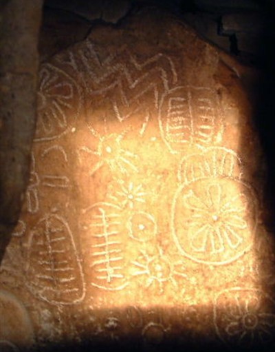 Tall view of equinox sunlight illuminating sun symbols, zigzags and ladder motifs on the Cairn T backstone at Loughcrew
