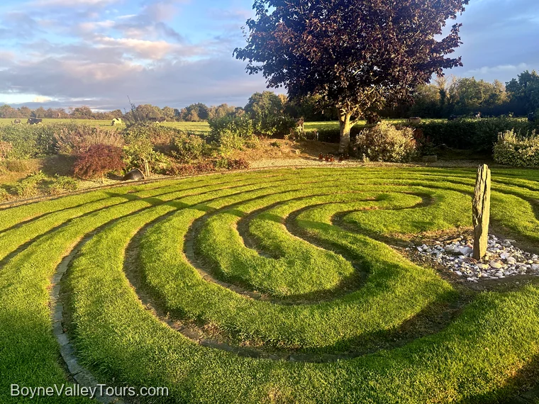 Grass labyrinth at September sunset with a long shadow from the standing stone stretching east to west across the circuits