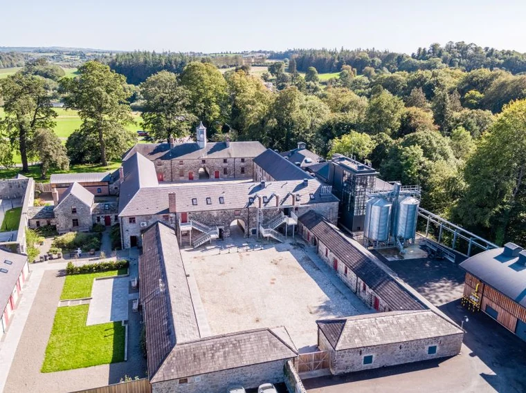 Aerial view of Slane Castle Distillery courtyard, stone stable buildings, clock tower and modern still house beside woodland