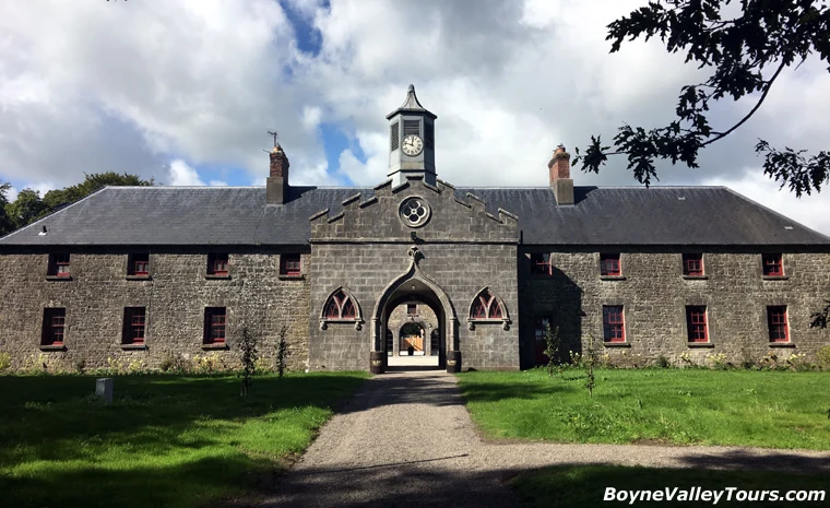 Historic stone stable yard entrance of Slane Castle Distillery with central archway, clock tower and red-framed windows